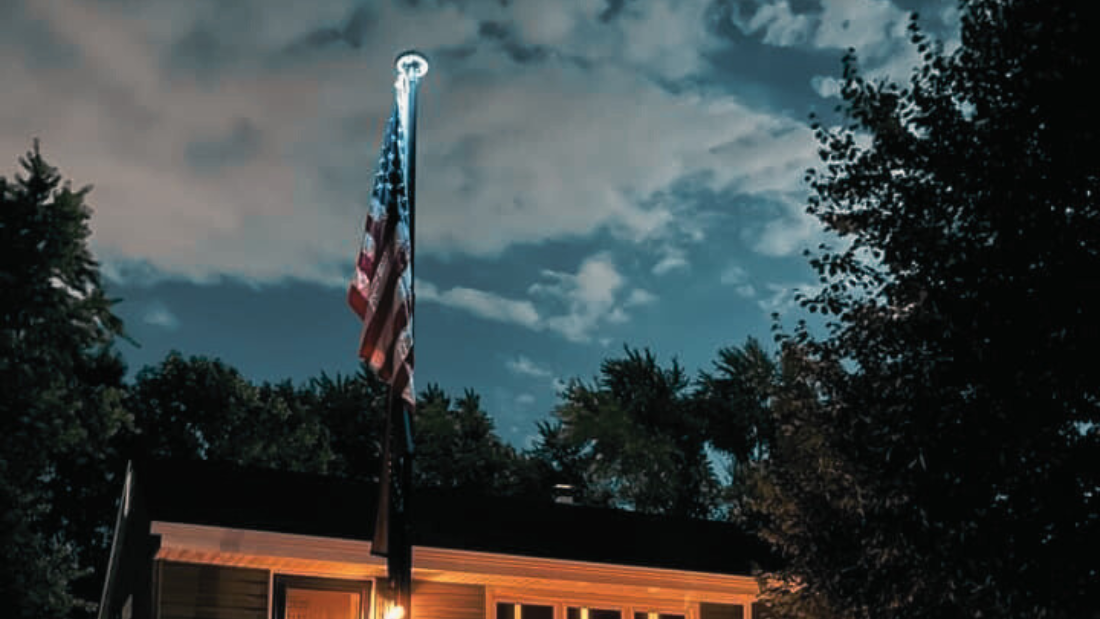 the american flag flying high at night illuminated by a led solar light lamp placed on top of a 25ft tall flagpole